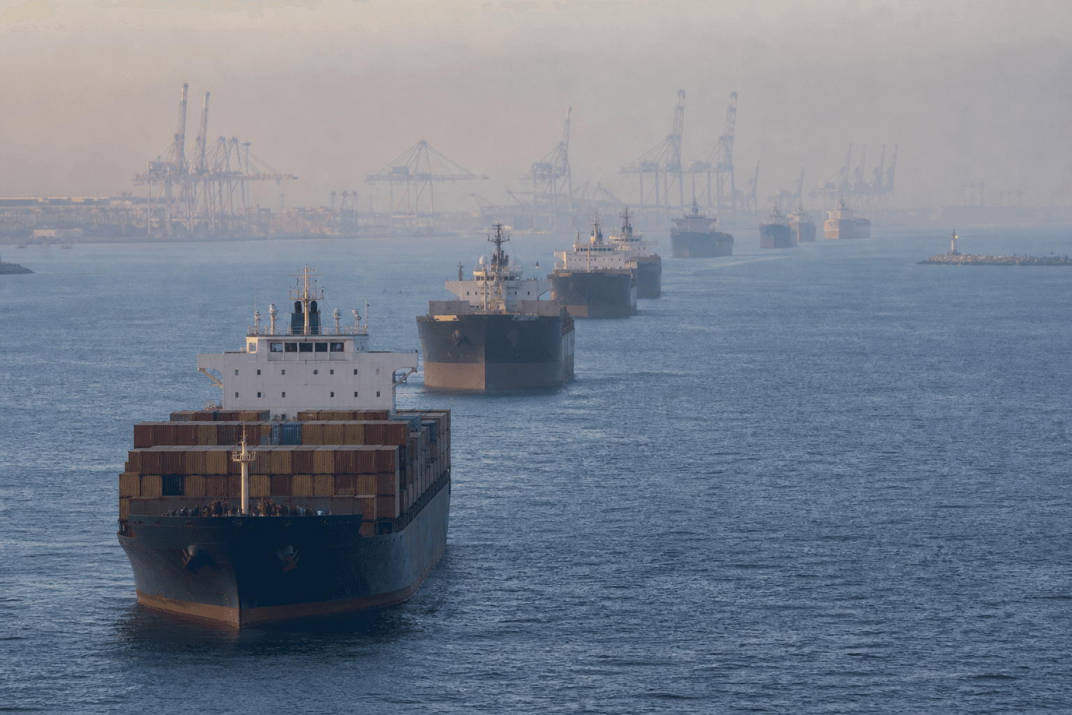 Commercial ships queue outside a container port in morning haze
